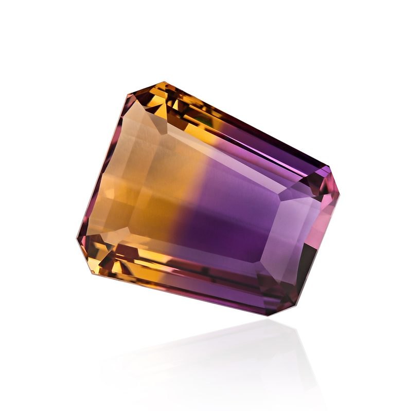 Faceted ametrine gemstone showing half purple amethyst and half golden citrine on neutral background