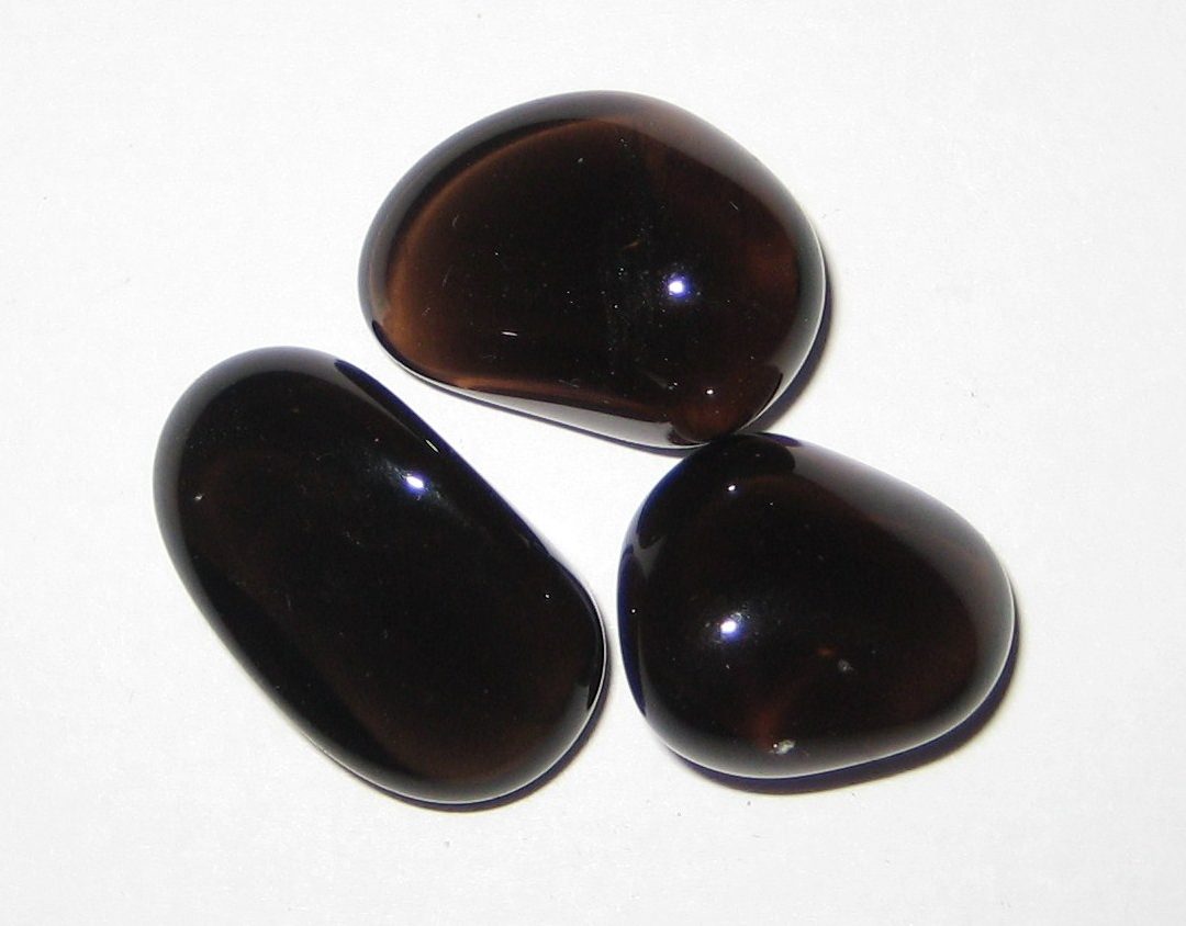 Apache Tears obsidian nodules showing translucent smoky brown glow when backlit against dark background