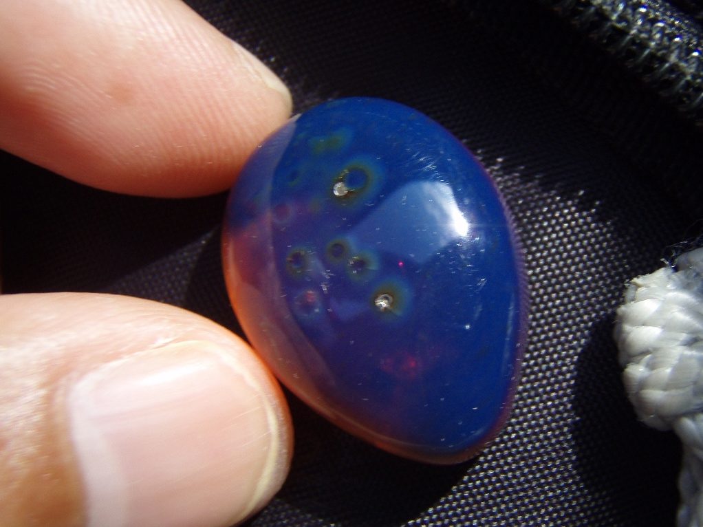 Blue amber specimen glowing vivid electric blue under UV light against dark background