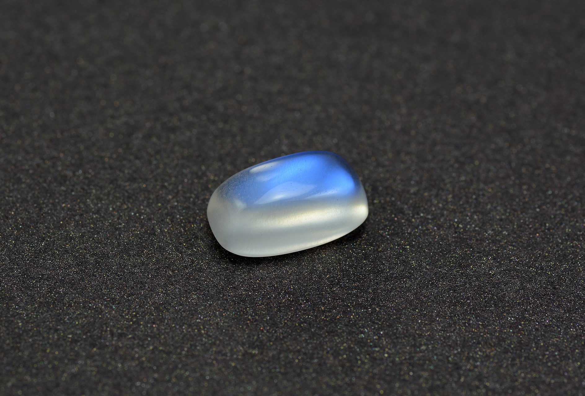 Blue moonstone cabochon showing intense blue adularescent glow rolling across white feldspar surface
