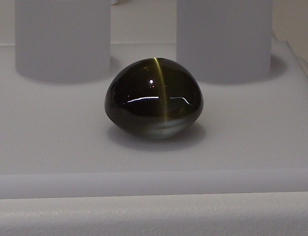 Chrysoberyl cat's eye cabochon showing sharp chatoyant beam on honey-yellow background under direct light