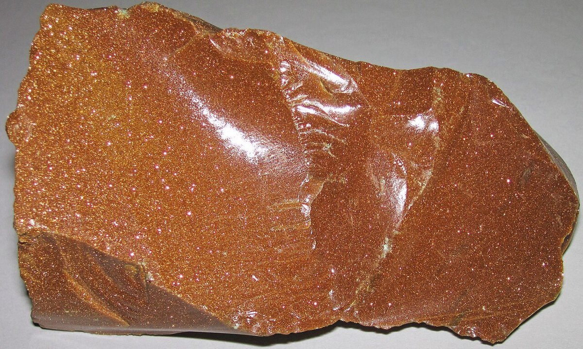 Polished goldstone cabochon showing reddish brown sparkle from embedded copper on neutral background