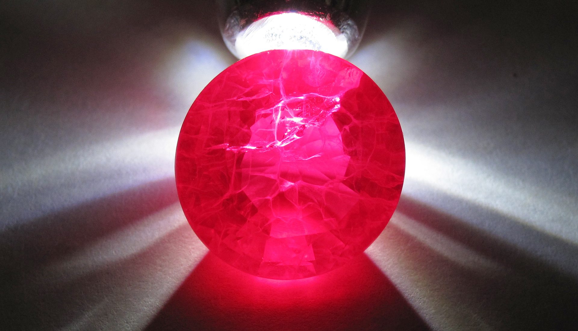 Lab Created Ruby faceted gemstone showing vivid red color against white background