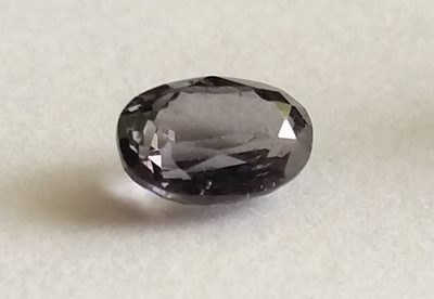 Faceted musgravite gemstone showing pale gray-violet color on a neutral background