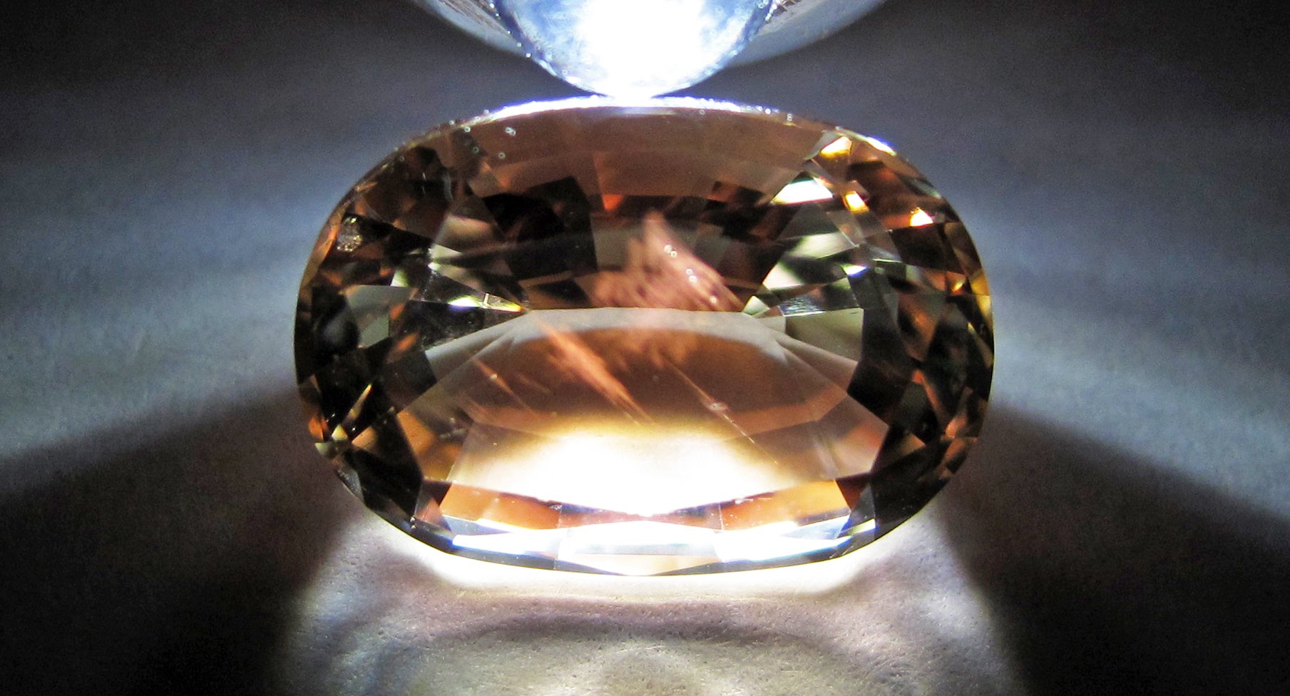 Faceted Oregon sunstone showing warm orange color with aventurescent copper schiller sparkle on white background