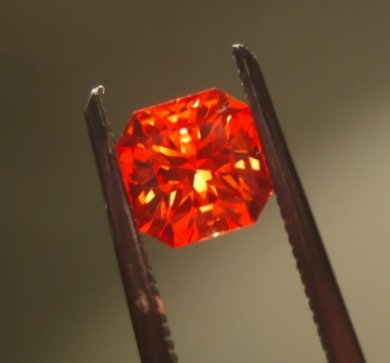 Faceted padparadscha sapphire showing salmon pink-orange color against white background
