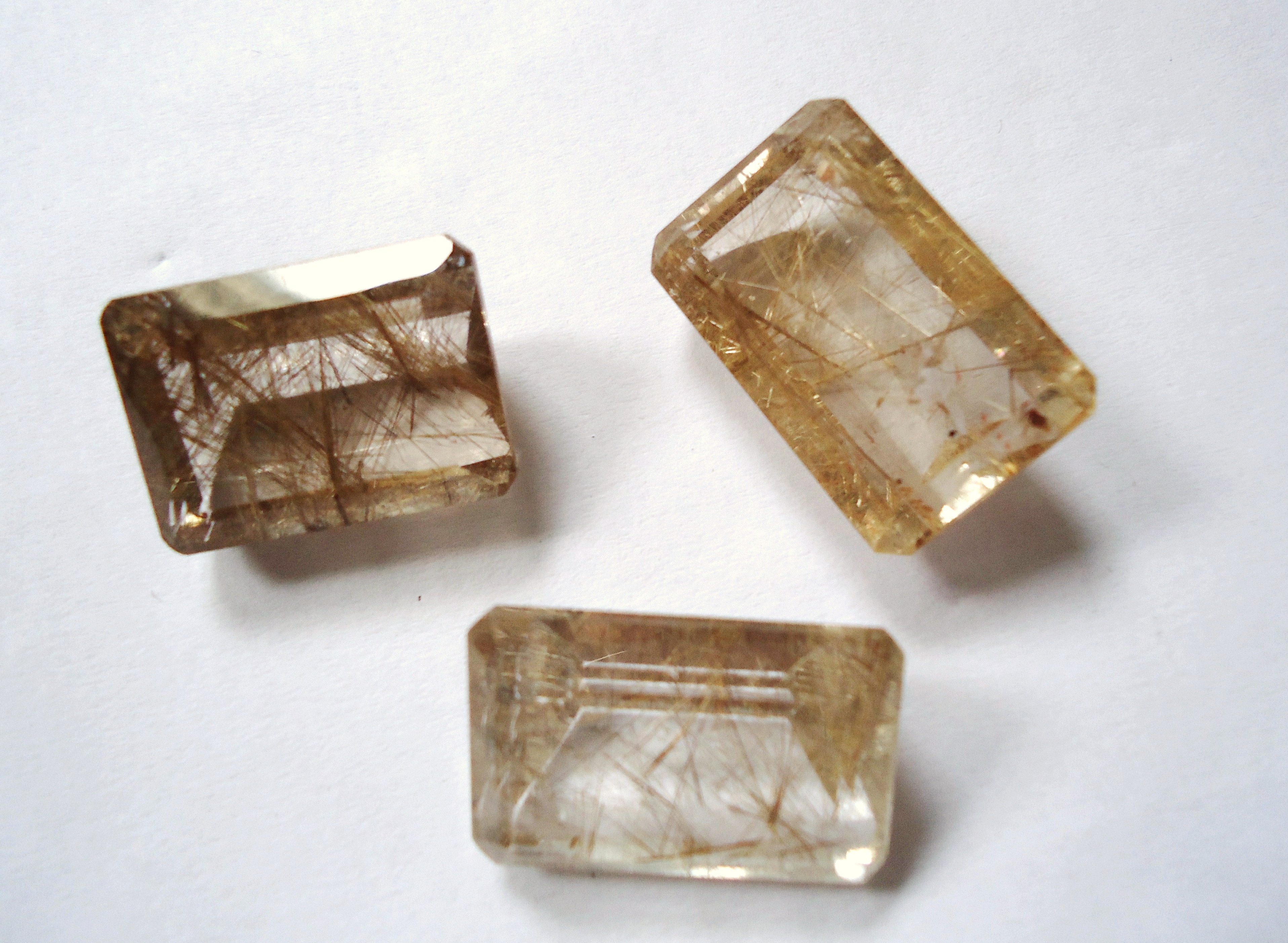 Rutilated quartz cabochon showing golden rutile needle inclusions on neutral background