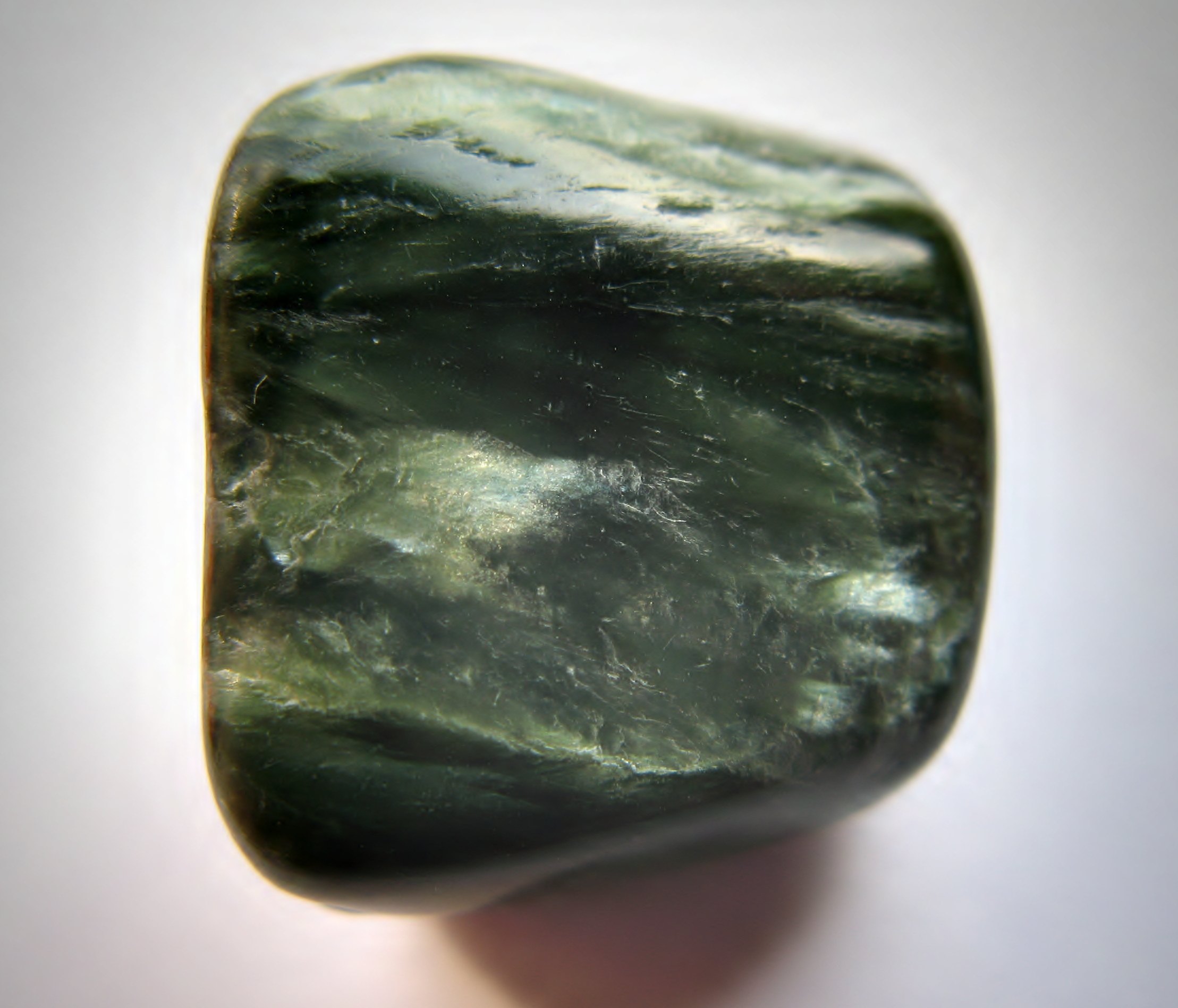 Polished seraphinite cabochon showing feathered silver on green chatoyancy on neutral background