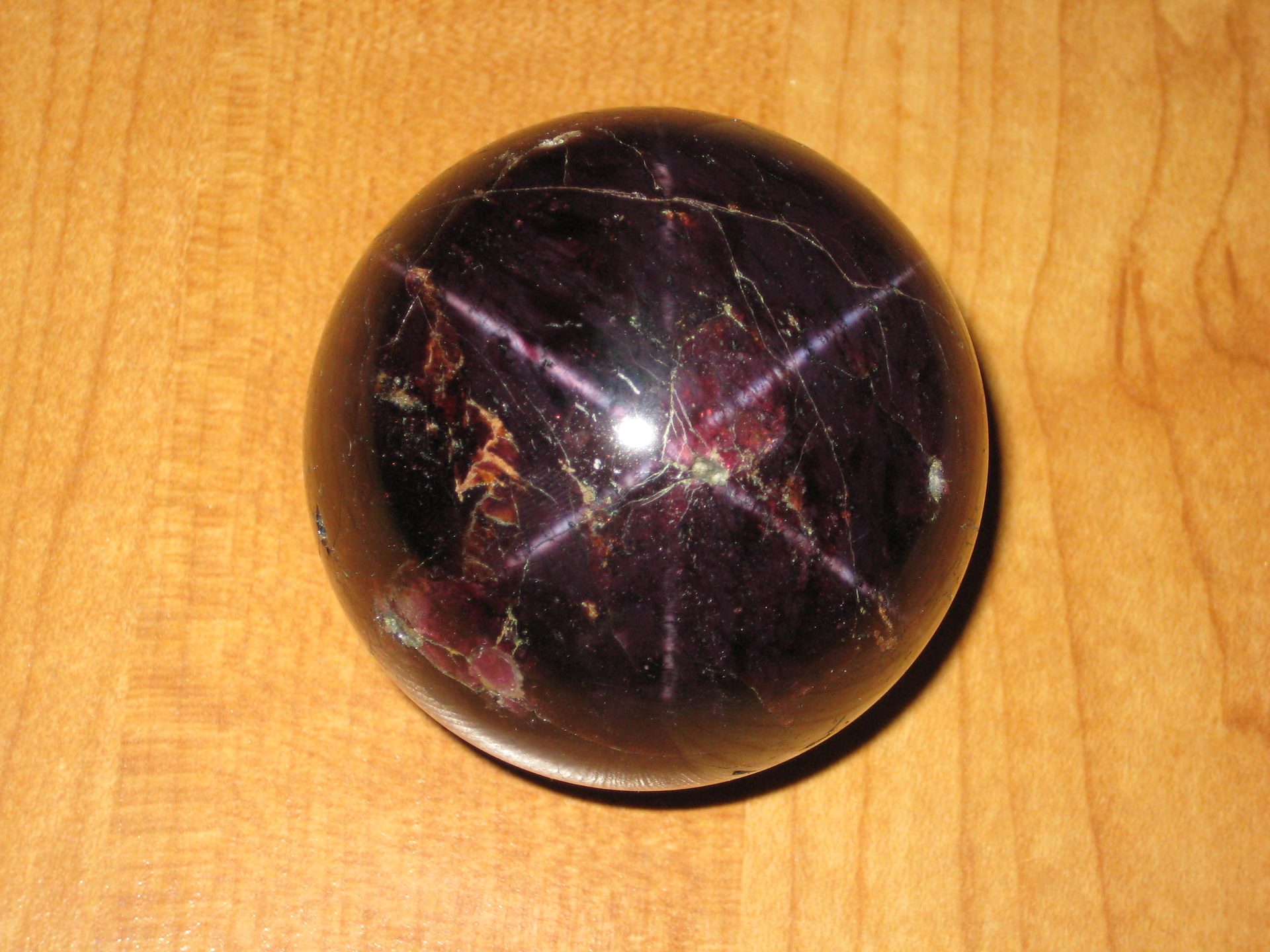 Star garnet cabochon showing vivid 4-rayed asterism star phenomenon on deep red almandine surface