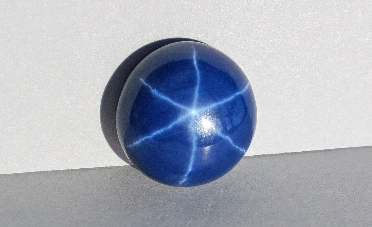 Polished blue star sapphire cabochon showing six-rayed asterism on deep blue body on neutral background