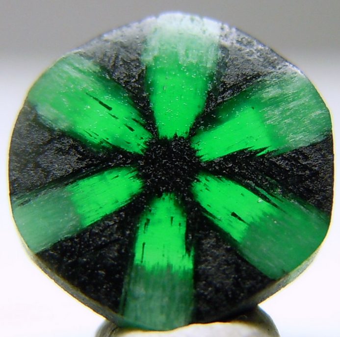 Trapiche emerald cross-section showing six-pointed dark carbon spoke pattern in green emerald